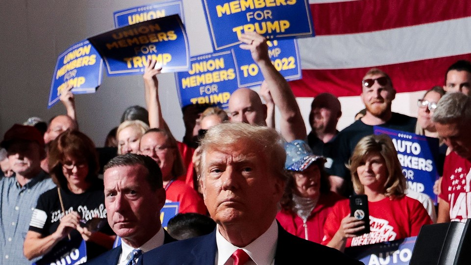 Trump in front of autoworkers holding signs.