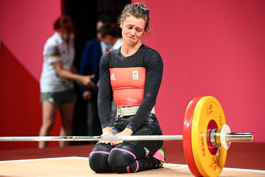 A weightlifter looks down toward a barbell with a pained look on her face.