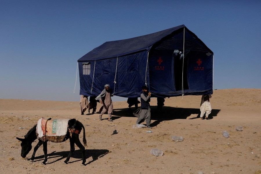 Seven people work together to carry a large fully-erected tent through a desert area.