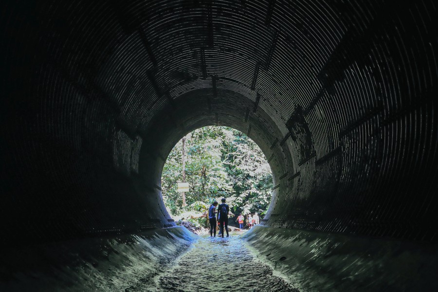 People stand near the opening of a large tunnel opening, with a small stream flowing through.
