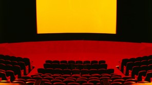 View of movie theater seats and screen, in black, red, and yellow