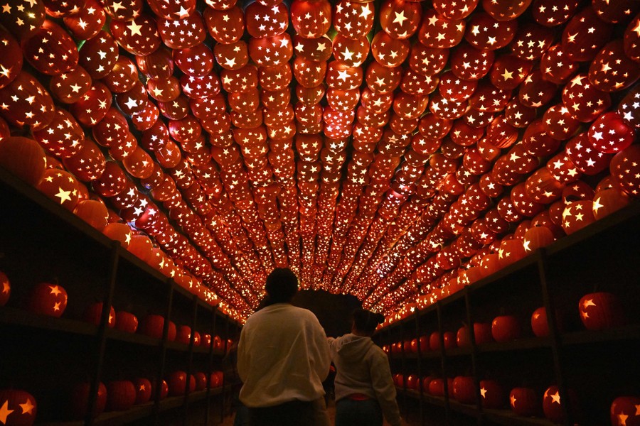 People walk beneath a long archway made up of carved and illuminated pumpkins.