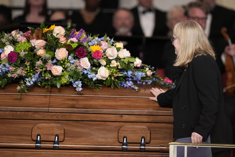 A person gently touches the side of a flower-covered casket during a funeral service.