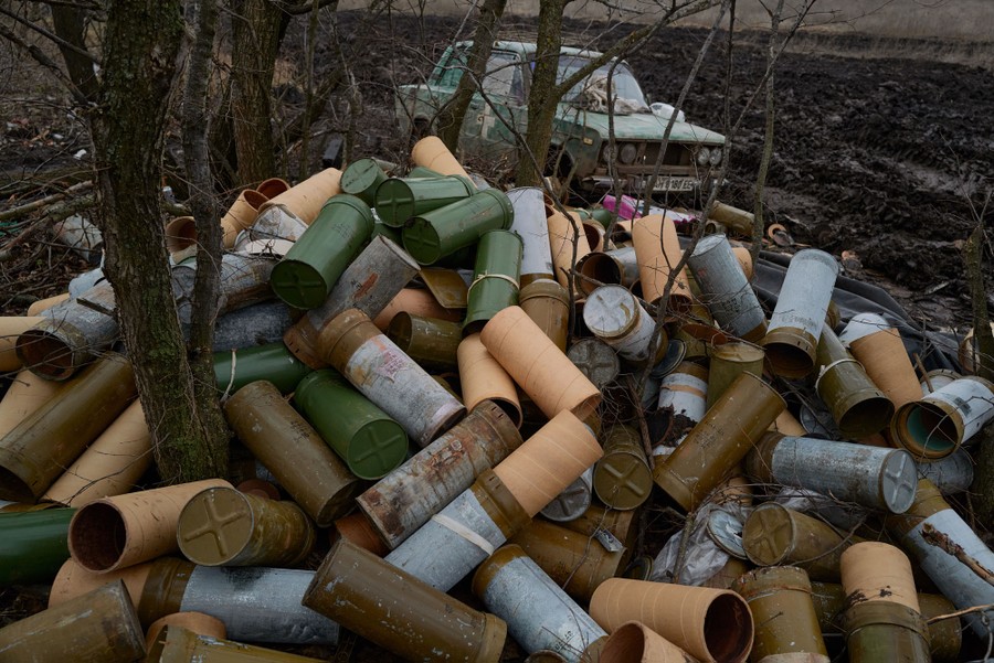 A large pile of empty ammunition shells sits among trees.