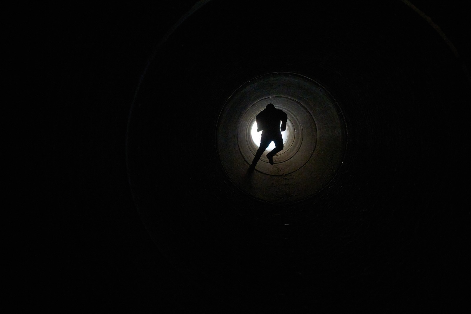 A boy runs inside a large cement pipe, seen from inside.