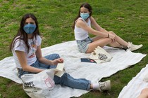 Three teenagers wearing masks sit apart on picnic blankets.