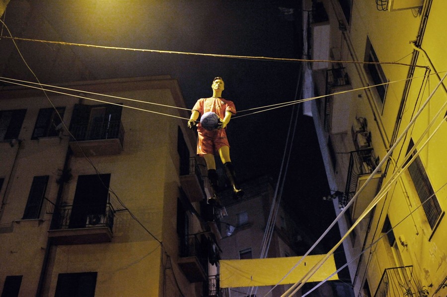 A dummy dressed as a soccer player is suspended above a street.