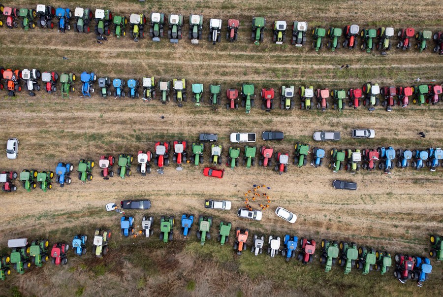 An aerial view of dozens of tractors parked in lines in a field