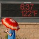 A person with an umbrella walking past an electronic sign showing the temperature to be 122 degrees Fahrenheit
