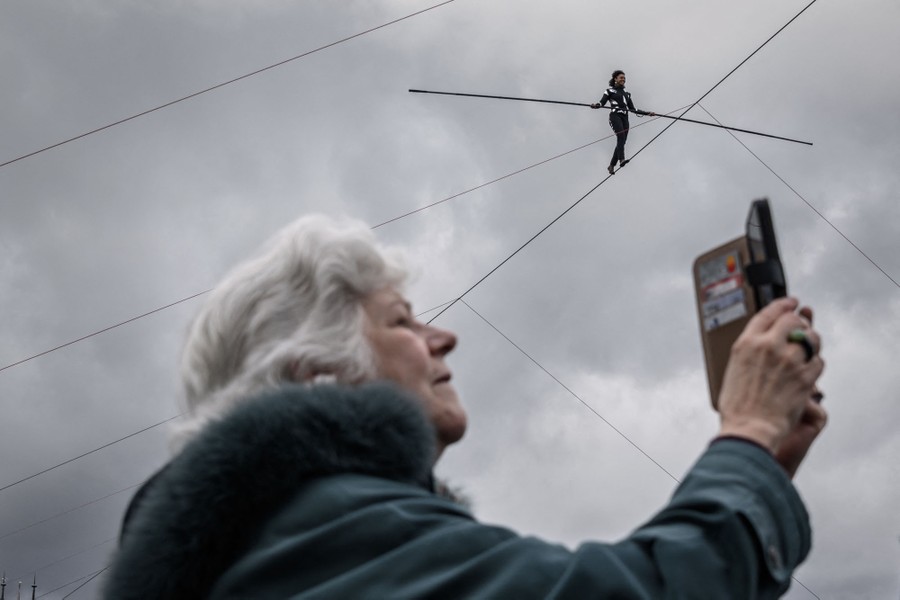 A person holds up their mobile device while a tightrope walker performs overhead.