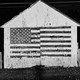 Black-and-white photo of a wooden house with the American flag painted on it