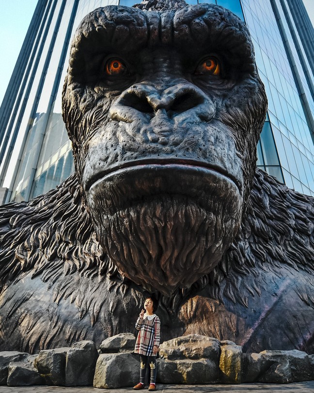 A child poses in front of a giant King Kong statue.