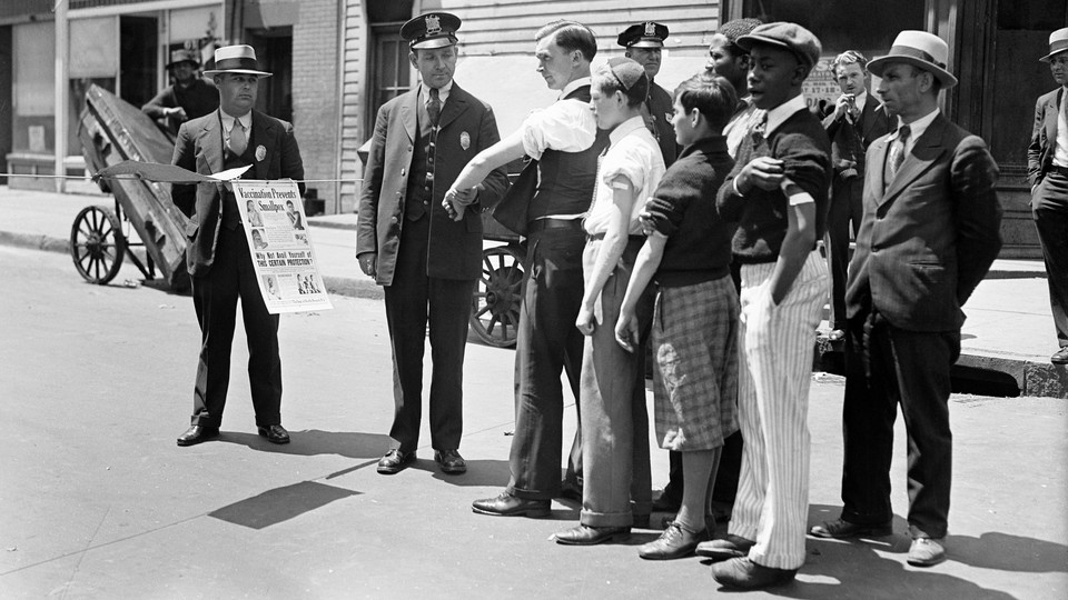 In a black and white photo, health officers at a checkpoint question people in line waiting to be screened to prevent spread of smallpox