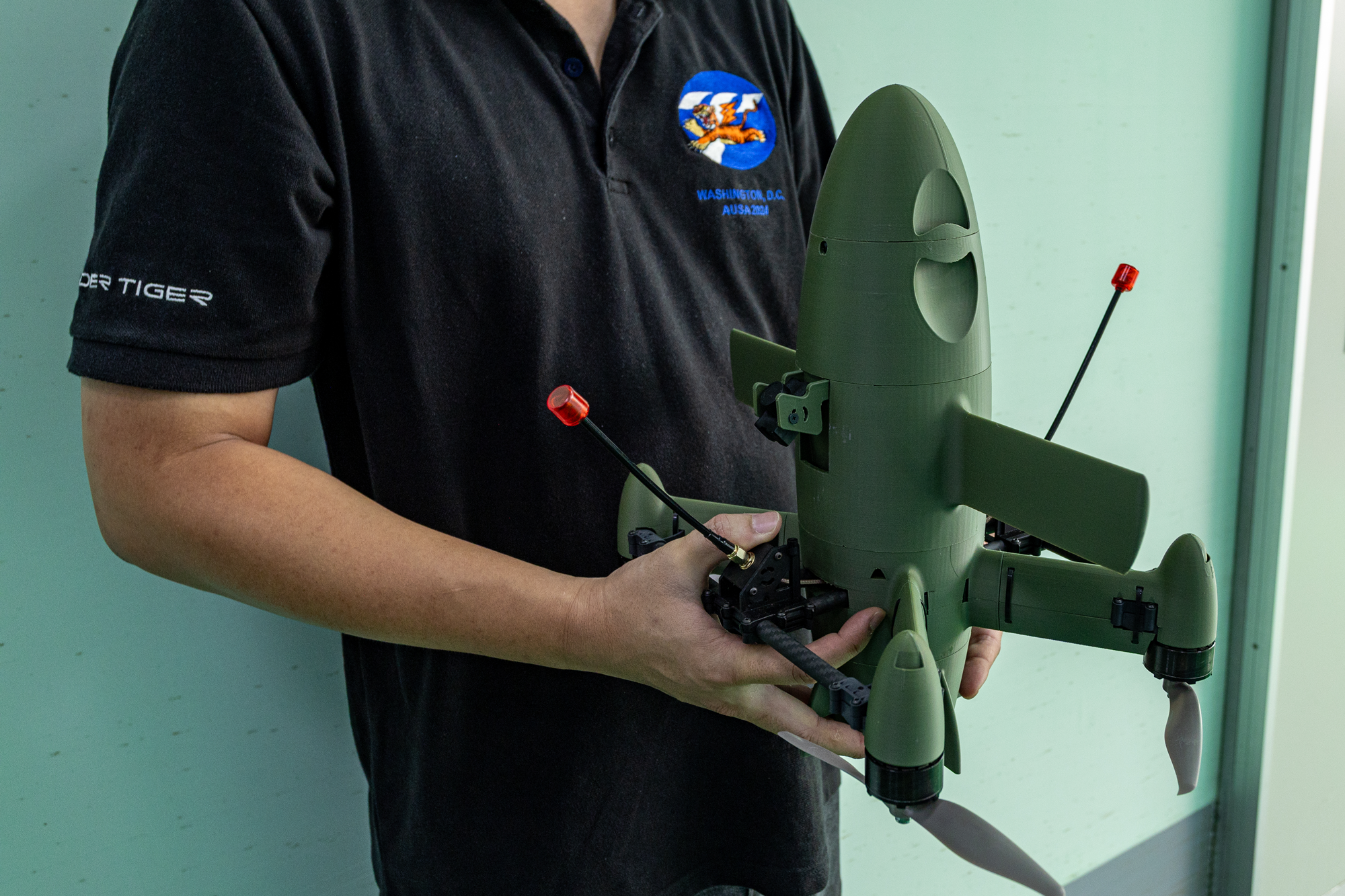 photo of torso of person in Thunder Tiger polo shirt holding olive-green torpedo-shaped drone with controller in 2 hands