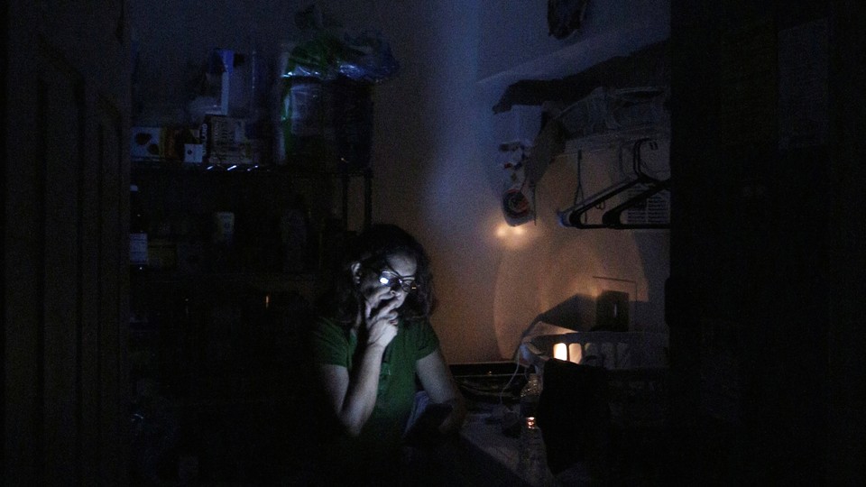 A woman reads from a mobile device in a dark room.