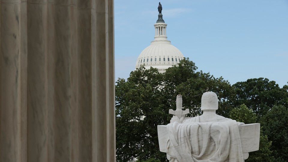 Photograph of a statue from the backside holding a sword. The U.S. Capitol Building is in the background, shrouded by trees.
