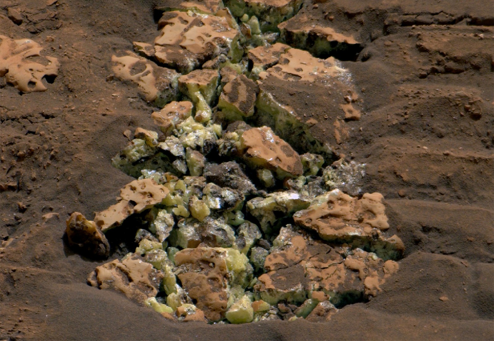 A crushed rock with exposed greenish-yellow sulfur crystals