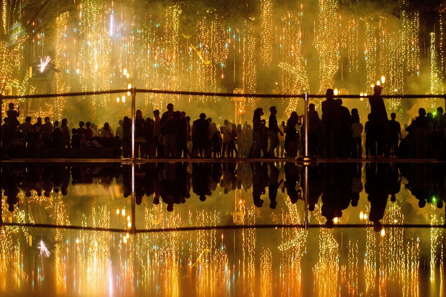A crowd of people stands and looks at bright holiday decorations hanging nearby.