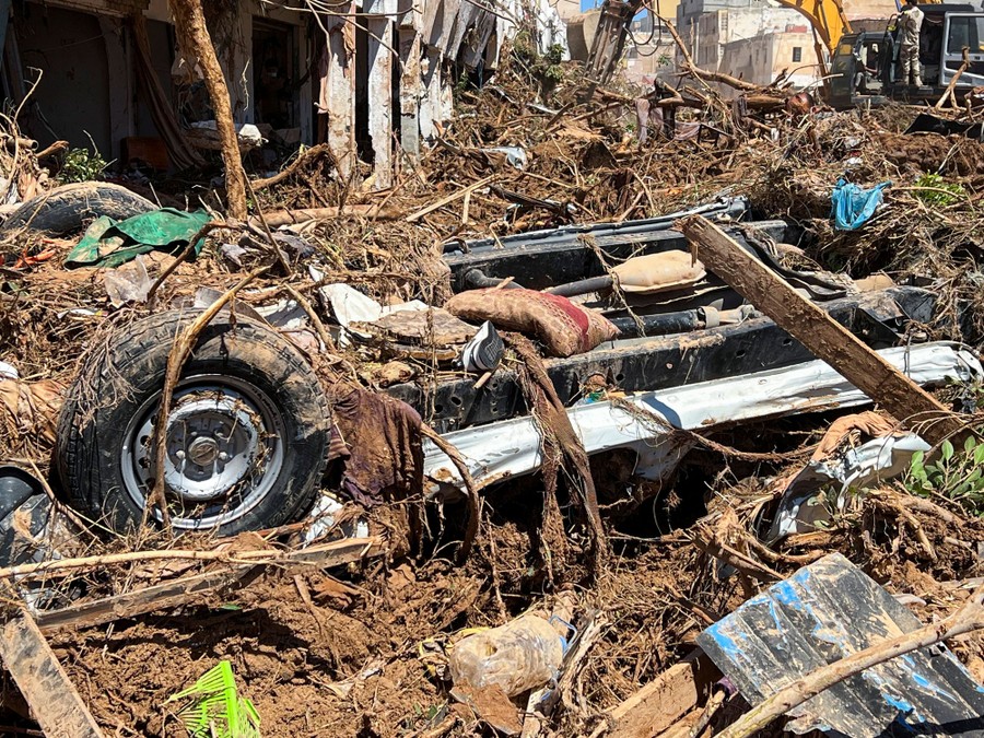 A wrecked car sits upside-down among piles of flood debris in a street.