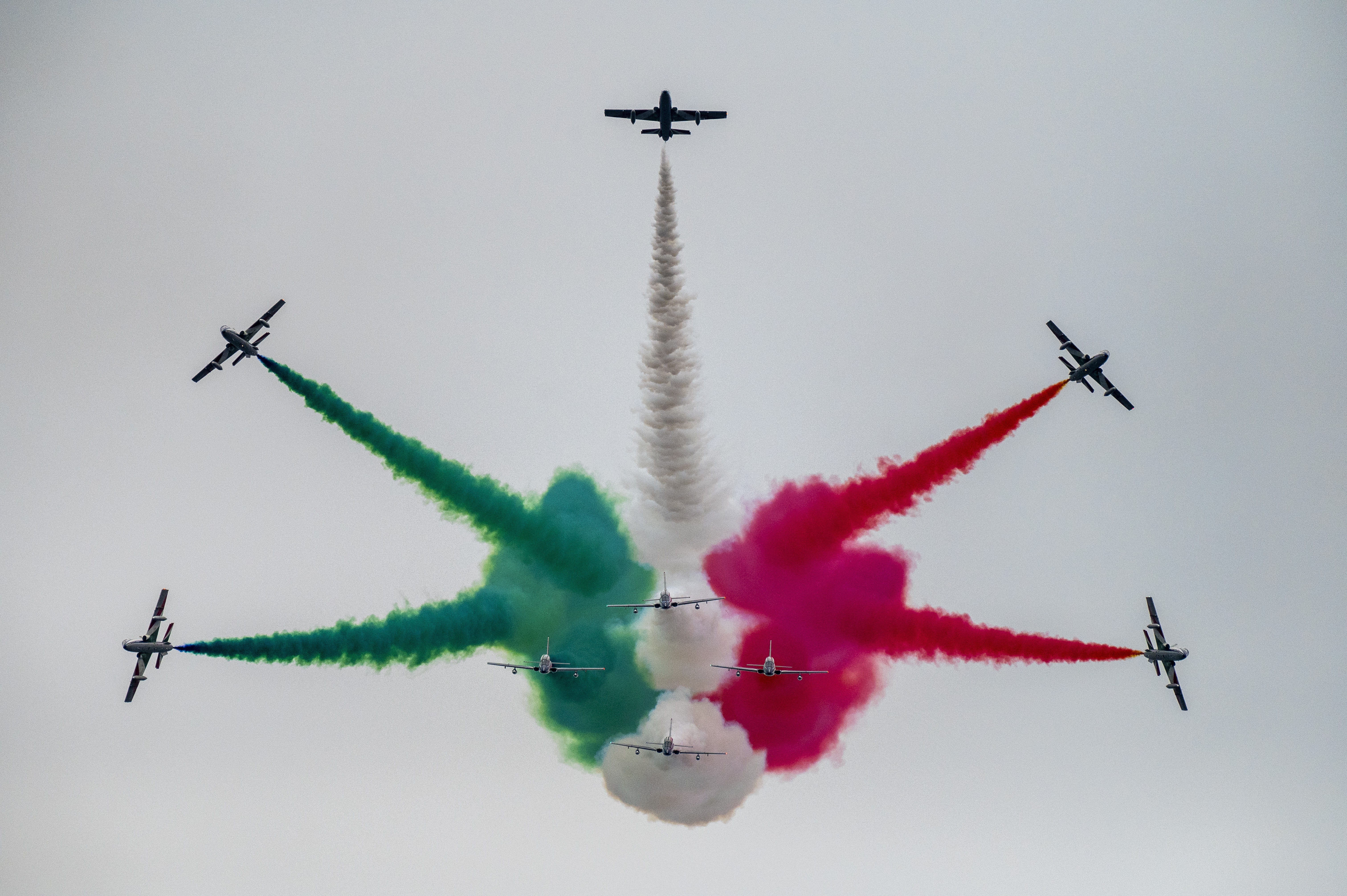 Nine fighter jets fly in formation, releasing green, white and red smoke.