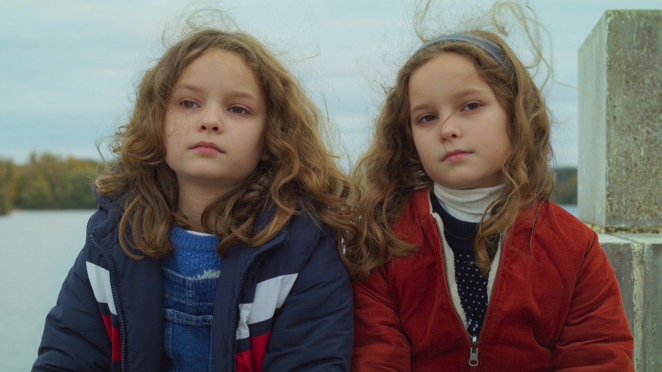 Joséphine and Gabrielle Sanz sitting together in front of a body of water in "Petite Maman"