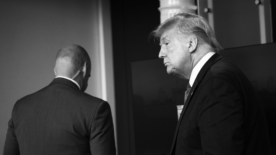 A black-and-white photo of Donald Trump in a suit with a security agent walking in front of him