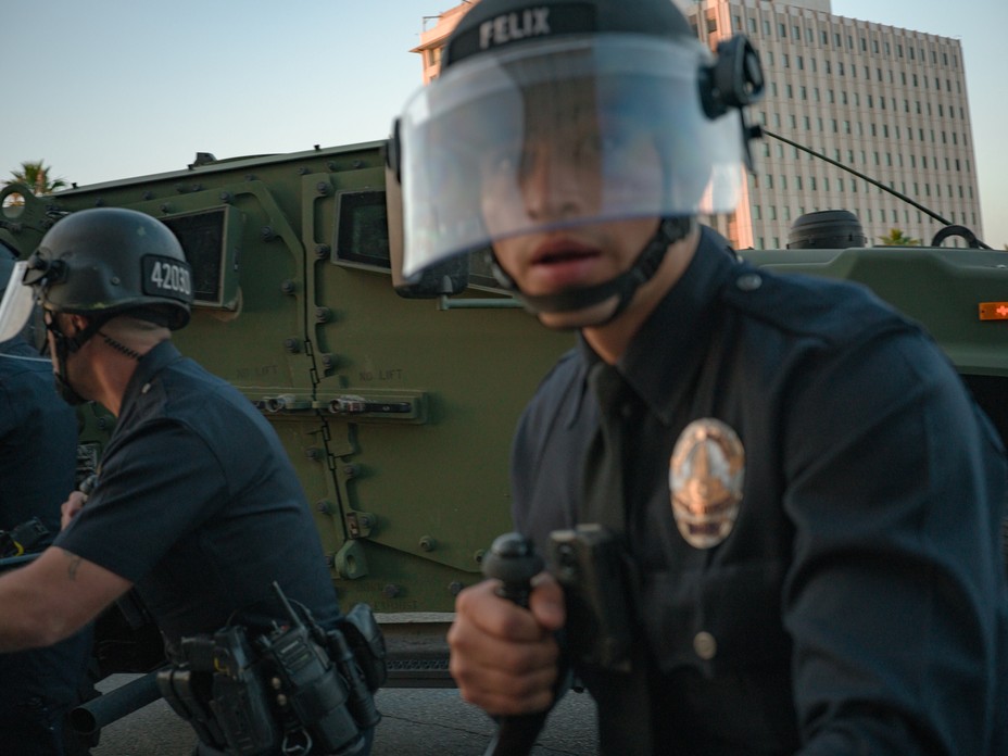 Police with shields approach with an armored vehicle in the background