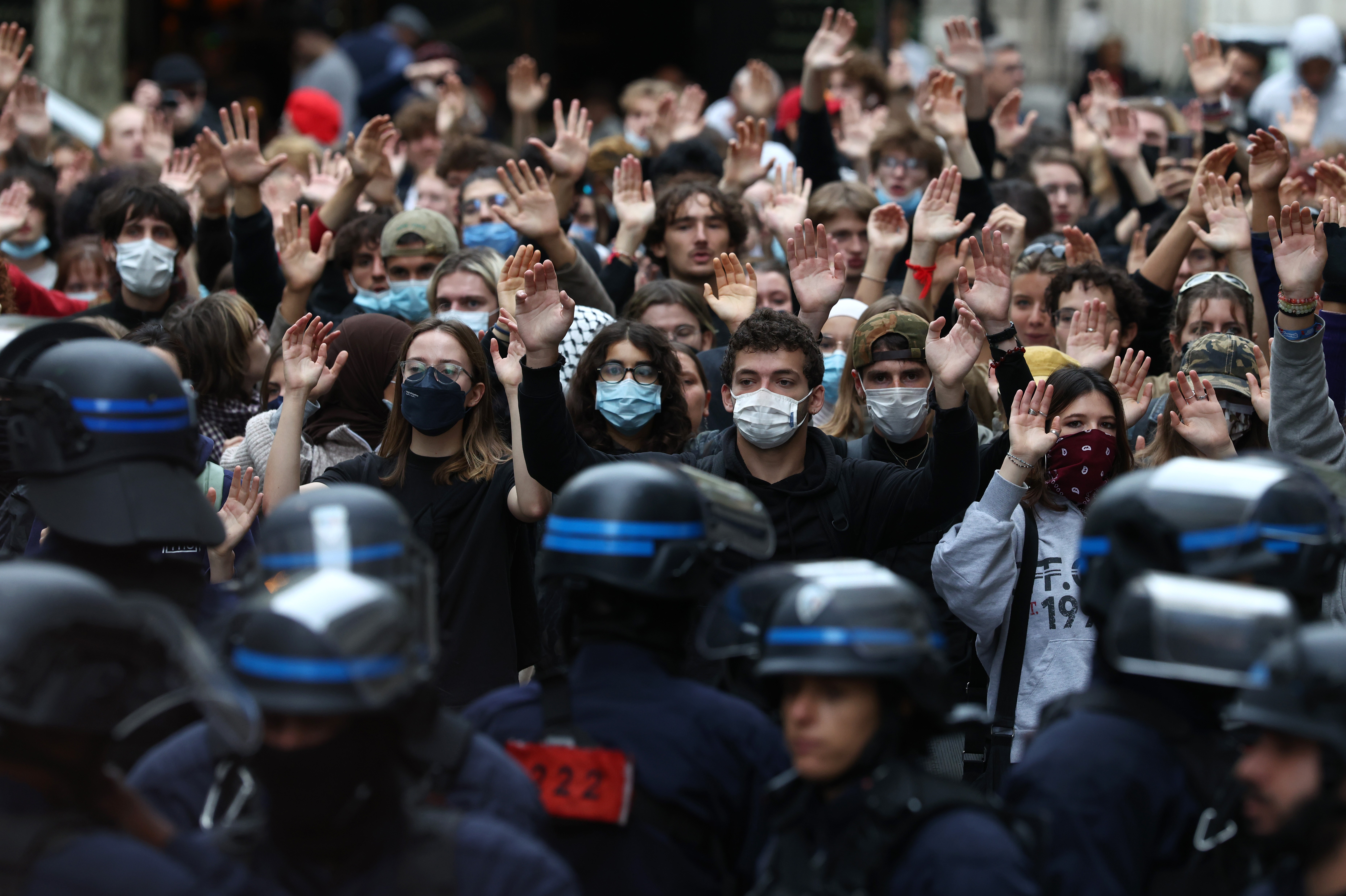 Protesting students raise their hands in front of riot police officers. 
