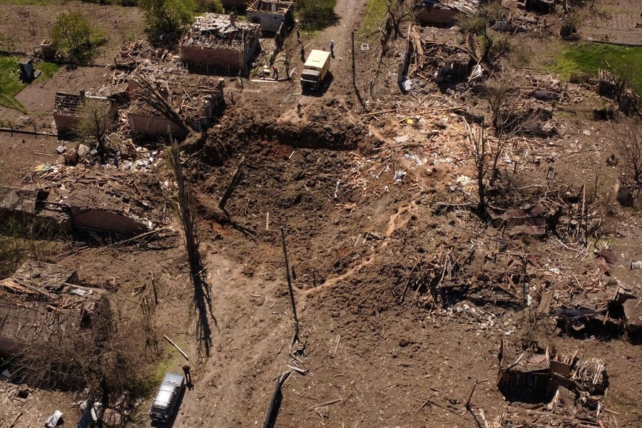 An aerial view of a crater in a road amid debris and damaged houses