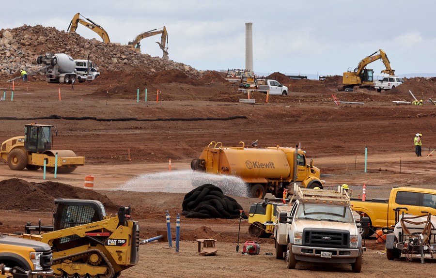 Trucks and construction equipment operate in a large open area.