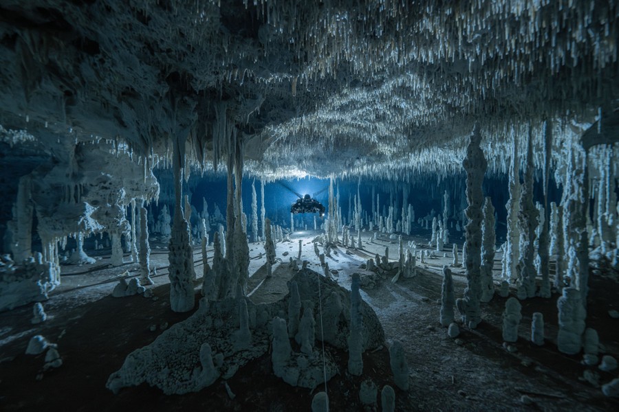 A diver using a rebreather glides through an underwater cave, which is lit dramatically.