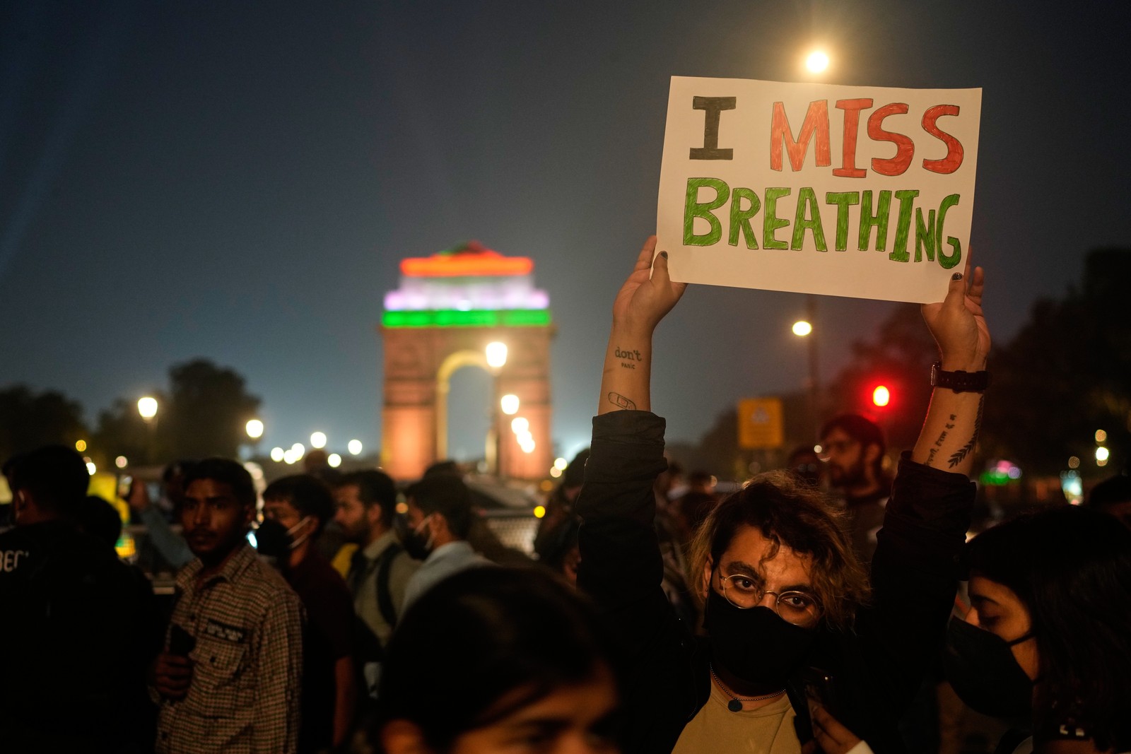 Protesters gather in a public plaza, with one holding a sign that reads 'I miss breathing.'