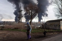 A woman walks in Odesa, Ukraine, as three large columns of smoke billow in the distance.