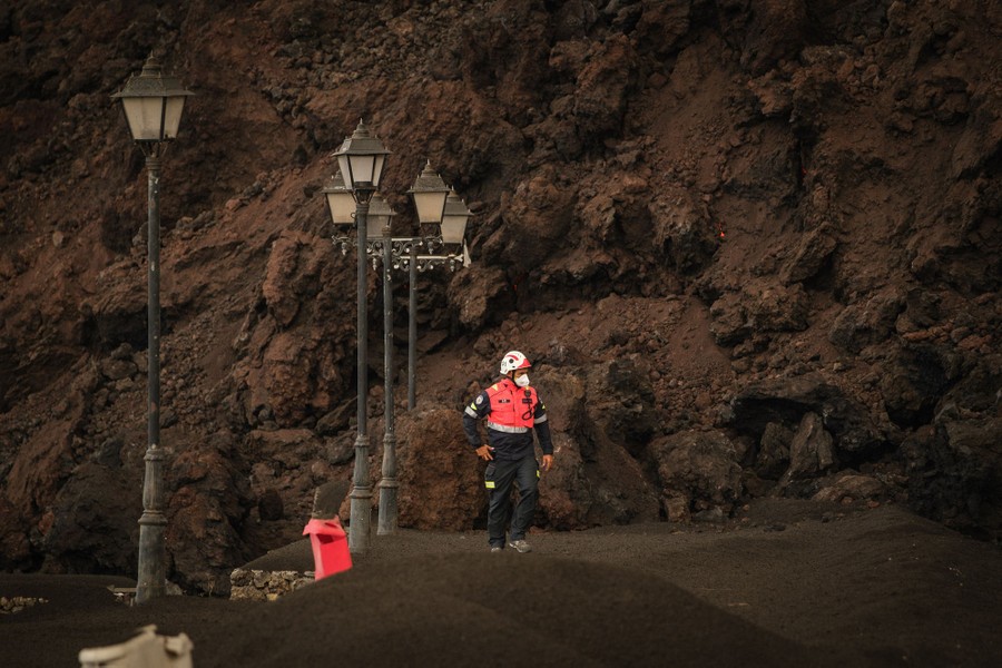 An emergency worker walks near a lava flow, on an ash-covered street.