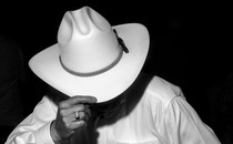 A man in a white shirt tilts the brim of a cowboy hat downward.