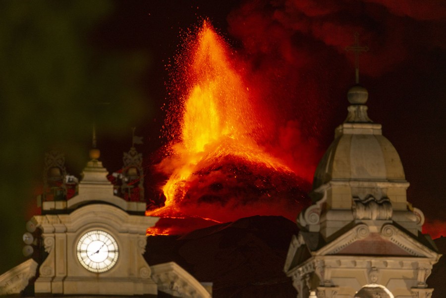 An erupting volcano is seen behind the rooftop of a church.
