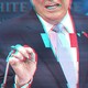 Photo of Donald Trump from the nose down speaking at a podium, with the image tinted red and blue as if glitching