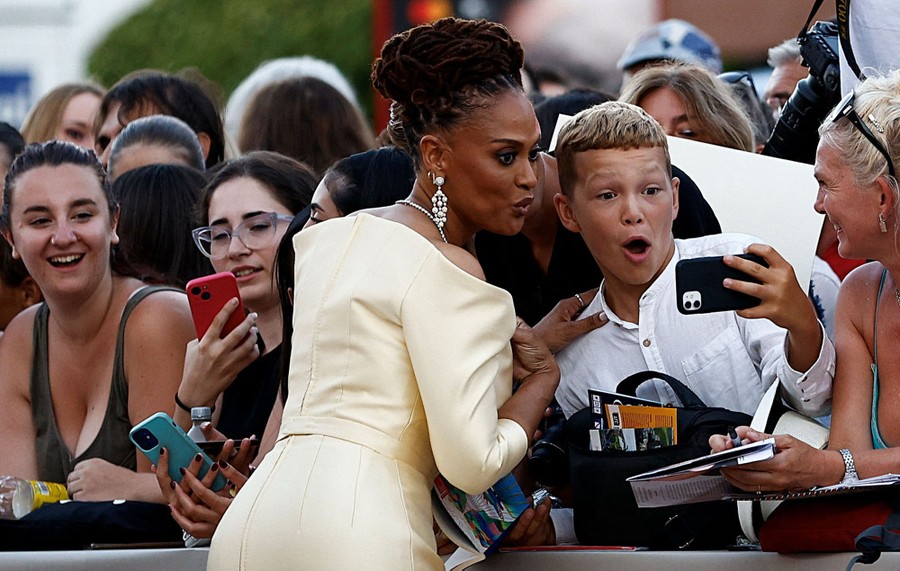A person poses with a fan for a selfie, among a crowd.