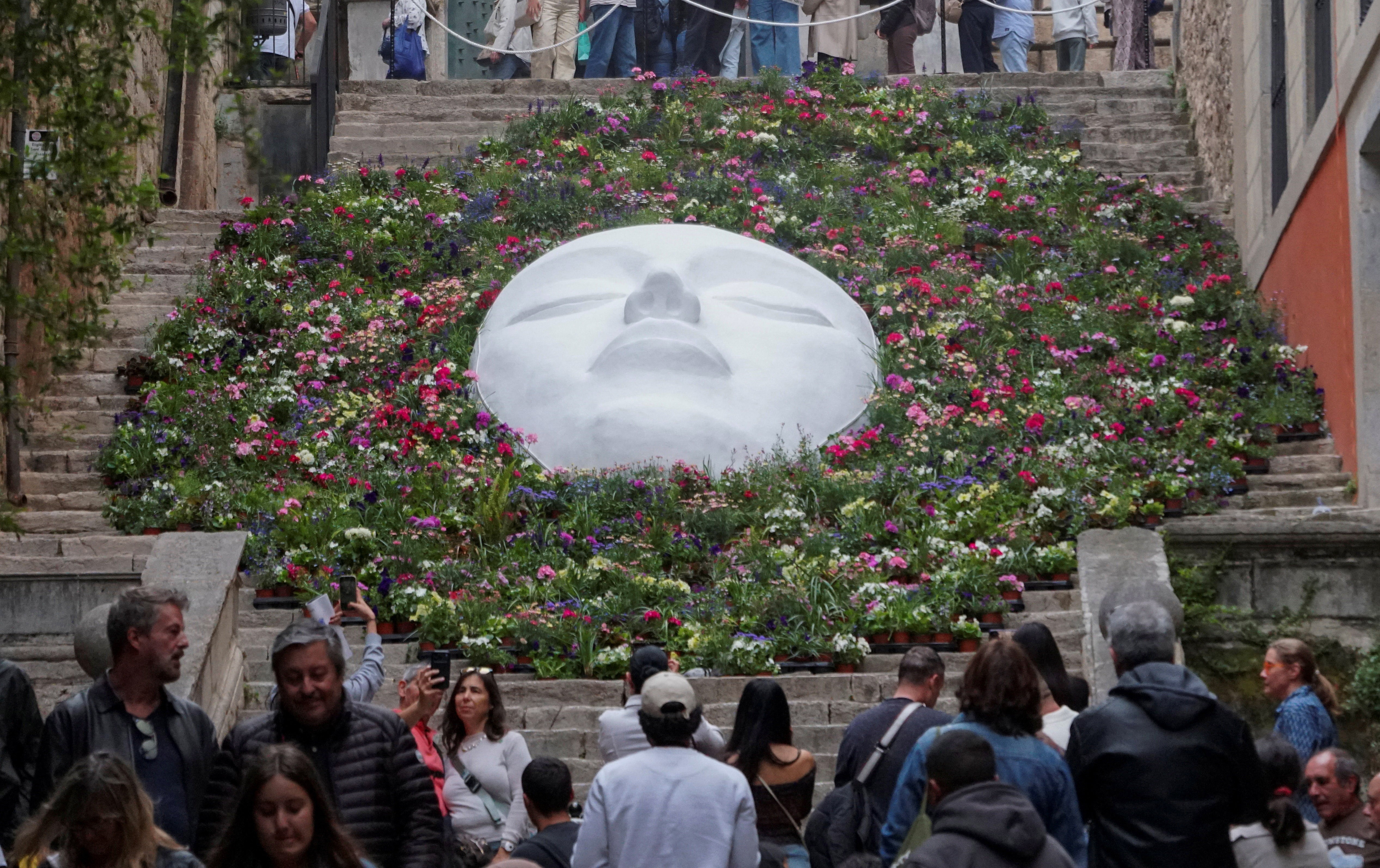 A large floral installation arranged on steps, surrounding a huge sculpture of an upturned face