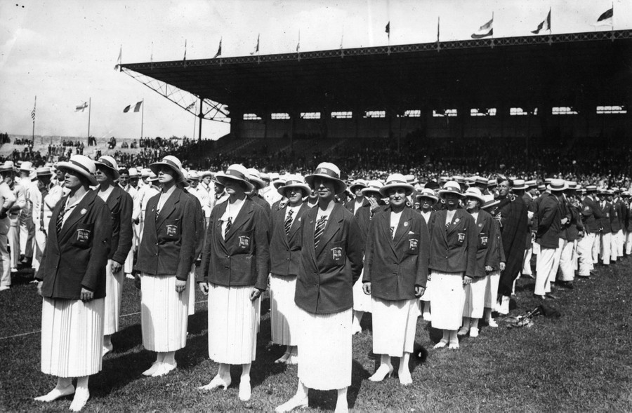 Athletes in dress uniforms stand in rows inside a stadium.