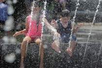 A girl in a pink tank top and a boy in a black tank top play in a fountain during a heat wave in Washington.