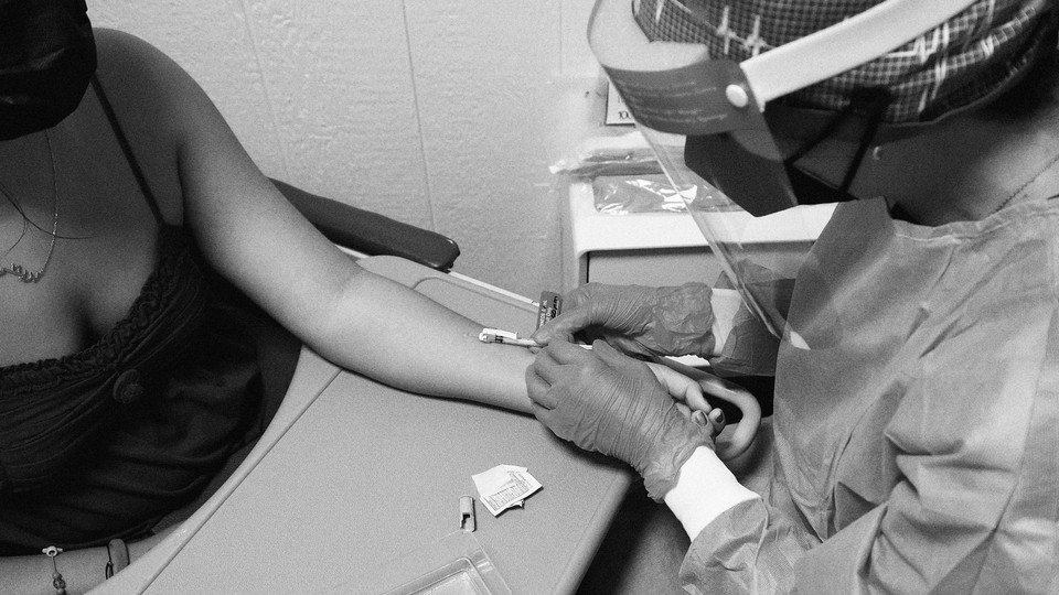 a masked healthcare worker injects a monkeypox vaccine intradermally into a woman's arm. the needle is entering almost horizontal to the arm so it can be shallow.