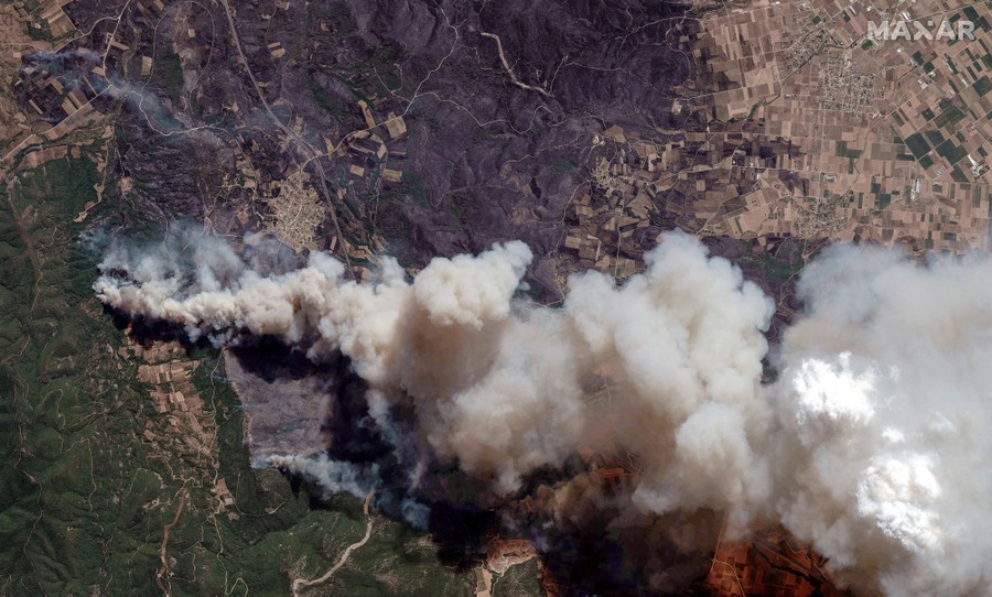 A satellite view of smoke rising from a fire, and a large swath of scorched ground