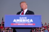 Picture of blurry Donald Trump standing at a lectern in the foreground, his audience in high-definition in the background