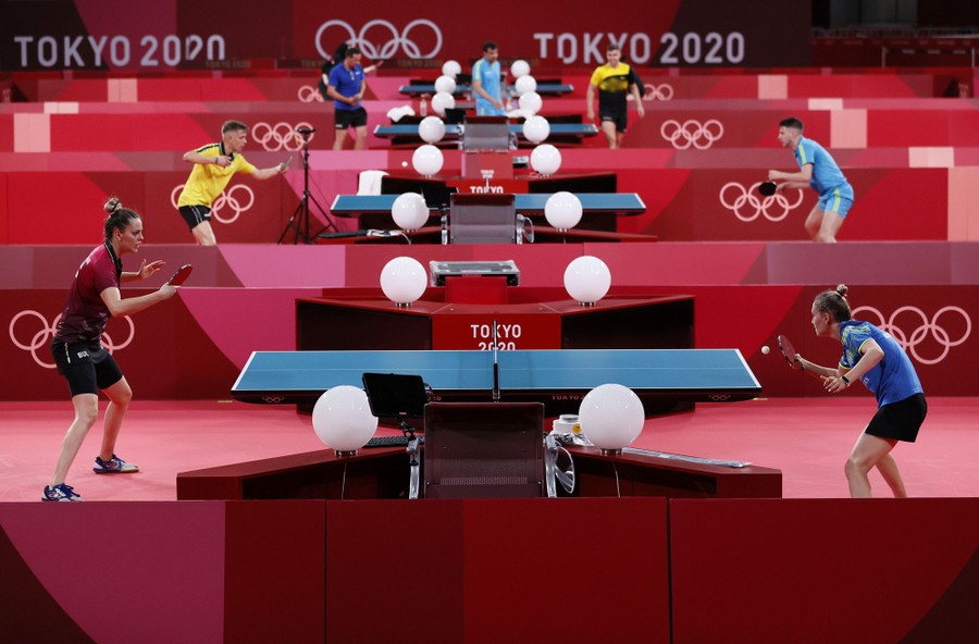 Table tennis players practice at four tables in an arena.