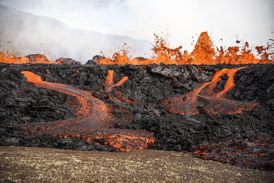 Lava erupts and flows across a valley floor.