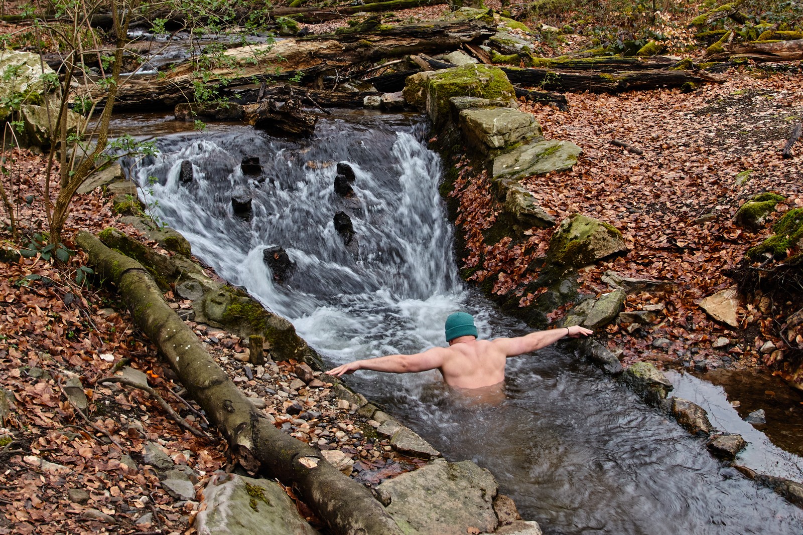 A shirtless man wades chest-deep in a running creek.