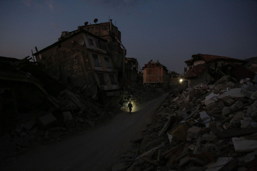 A person walks among quake-destroyed buildings at night.