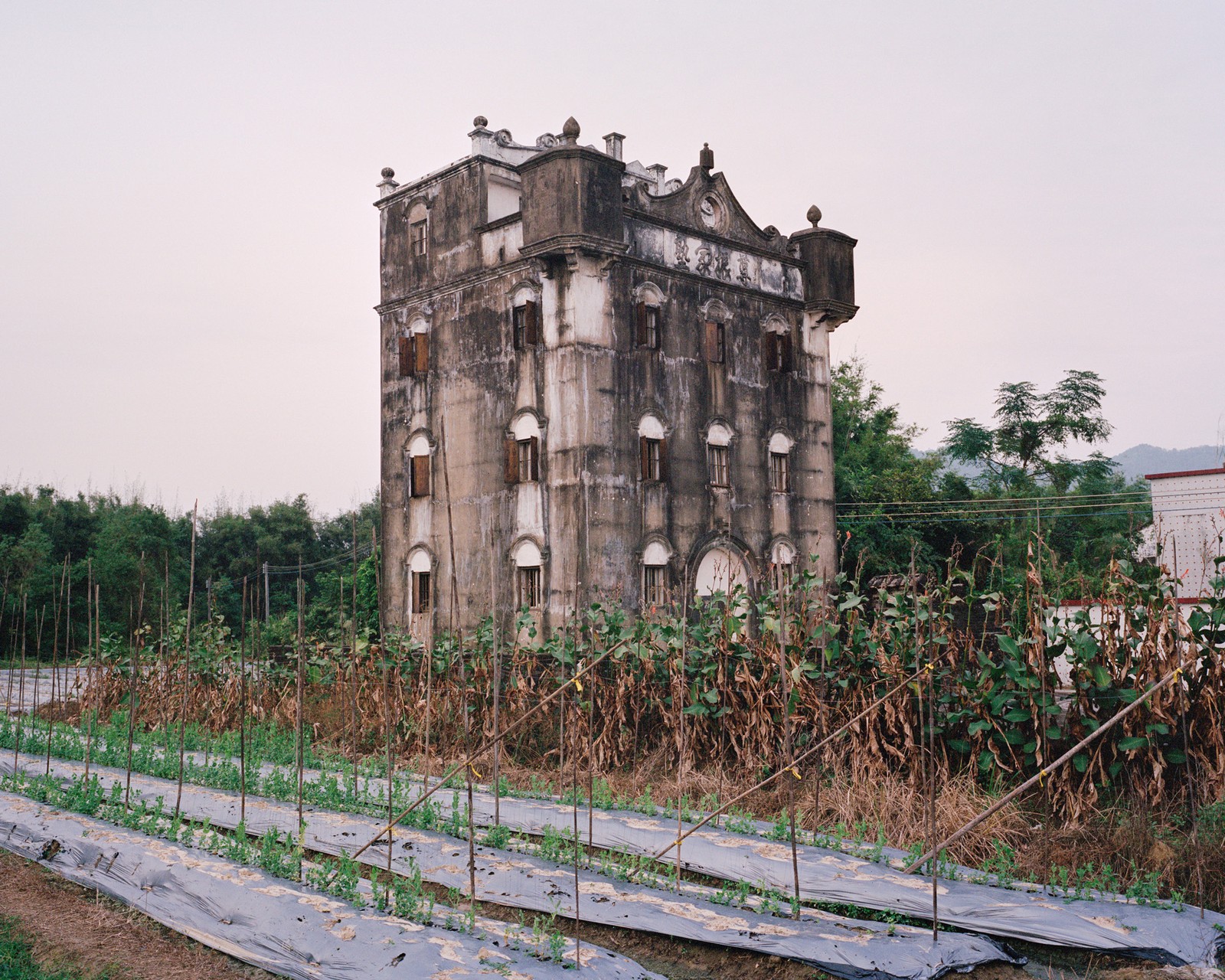A weathered four-story watchtower stands above a field and smaller buildings.