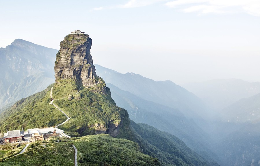 A building stands high atop a a stone pillar, with a small path leading to the summit.